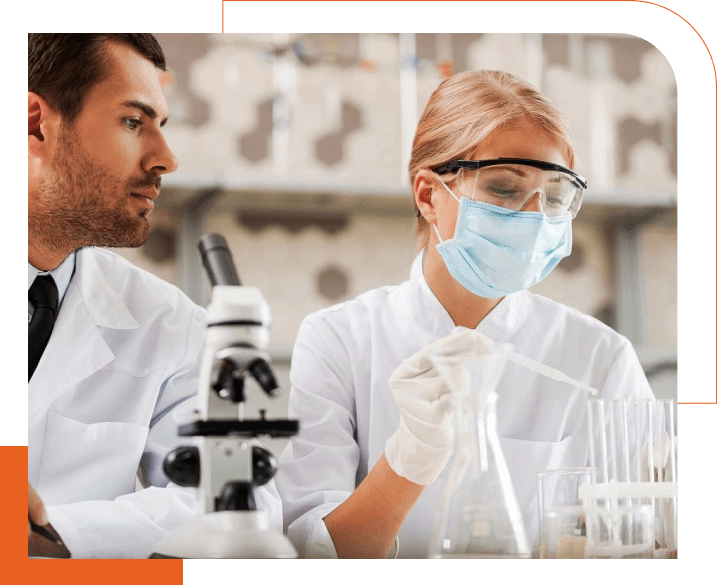 Two people in lab coats and masks working with a microscope.